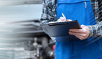 Car mechanic checking a car engine and writing on clipboard; panoramic banner